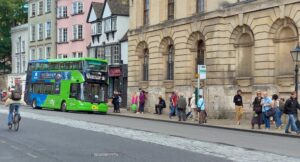 An Electric Bus a cyclist and about fifteen pedestrians in Oxford High Street