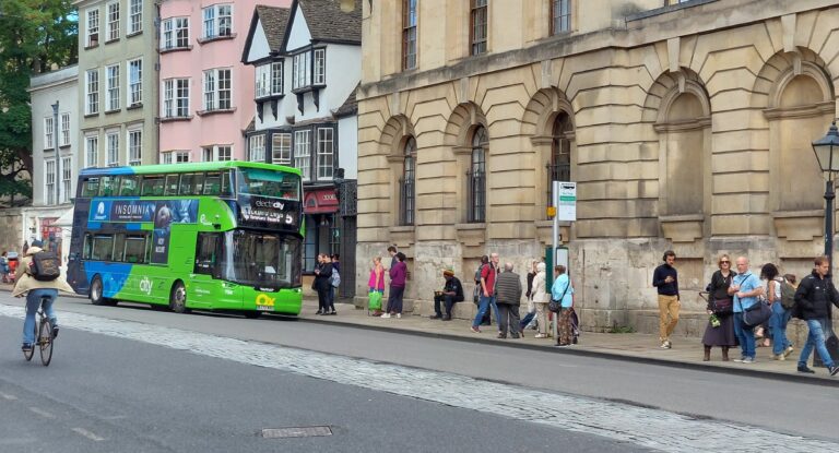 An Electric Bus a cyclist and about fifteen pedestrians in Oxford High Street